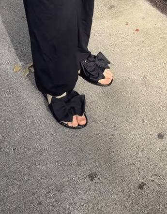 Person wearing black sandals with ruffled straps on a concrete surface