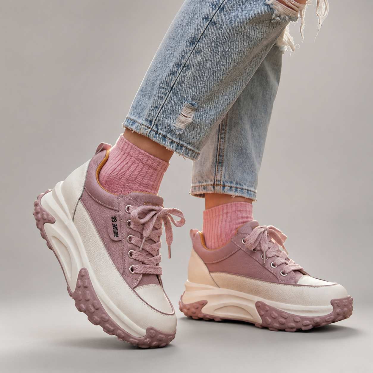 Pink sneakers with white soles worn with ripped jeans and pink socks on a gray background