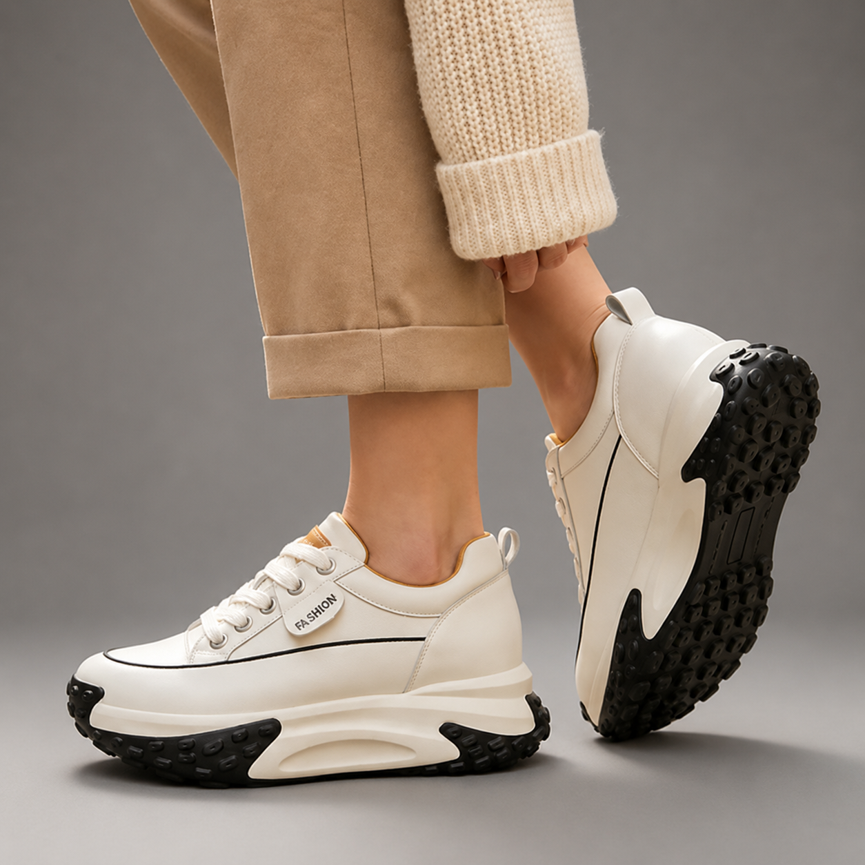 White sneakers with black soles worn by a person on a gray background