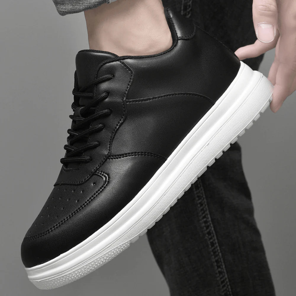 Black leather sneaker with white sole held by a hand against a gray background