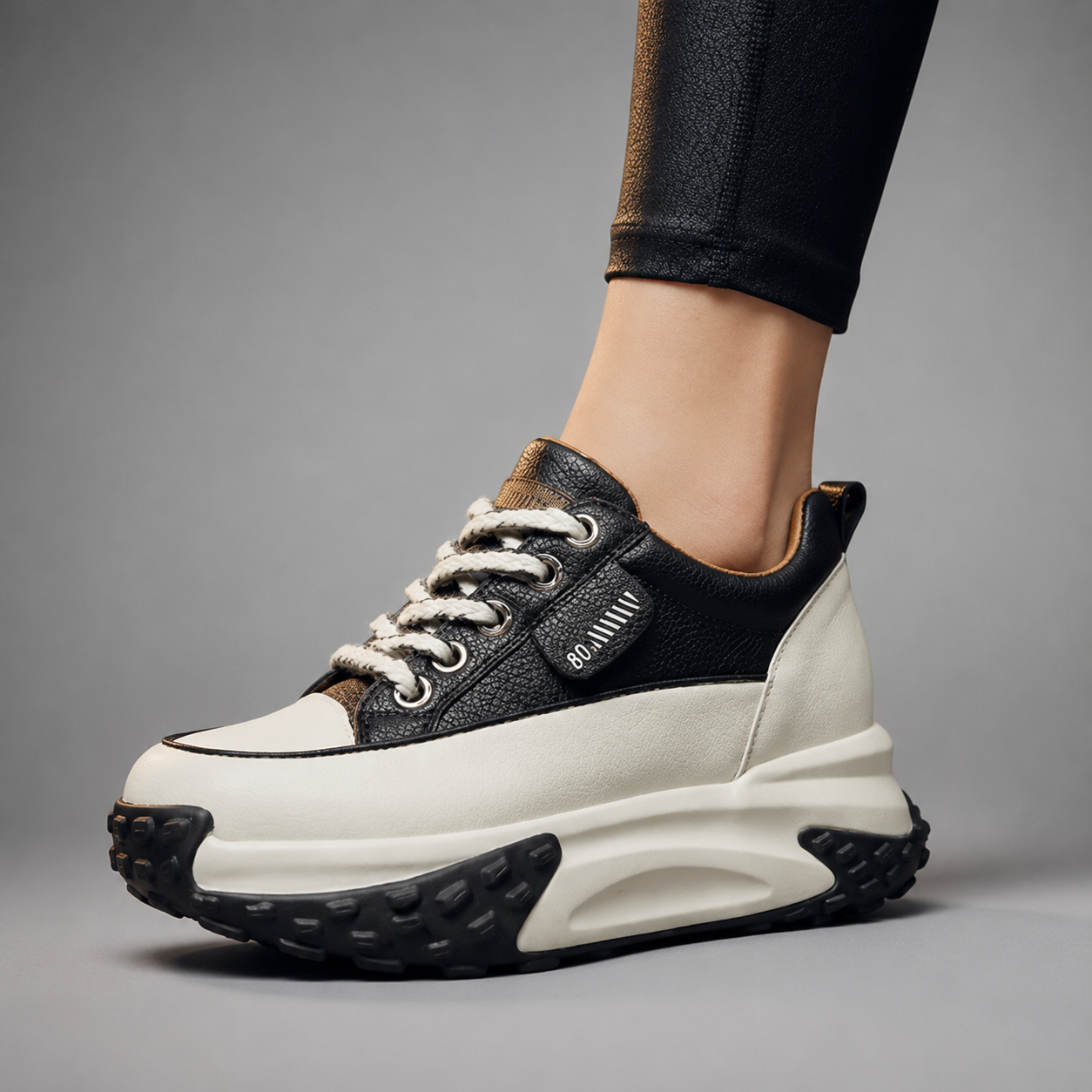 Black and white sneaker worn by a person on a gray background