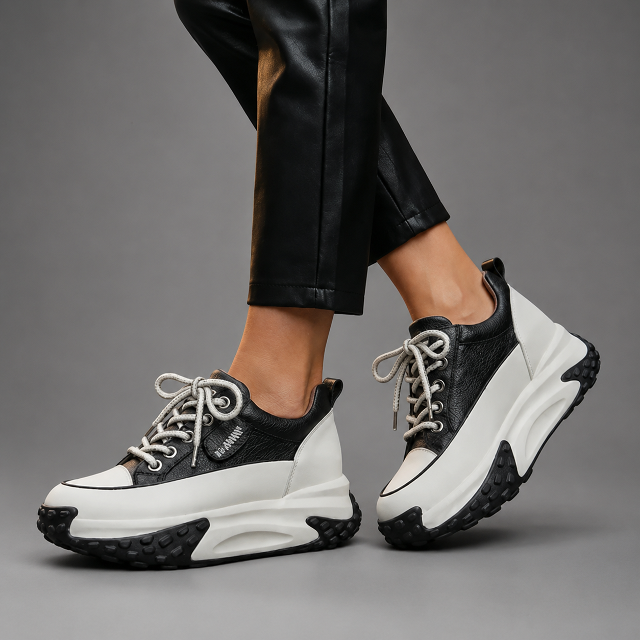 Black and white sneakers worn with black pants on a gray background