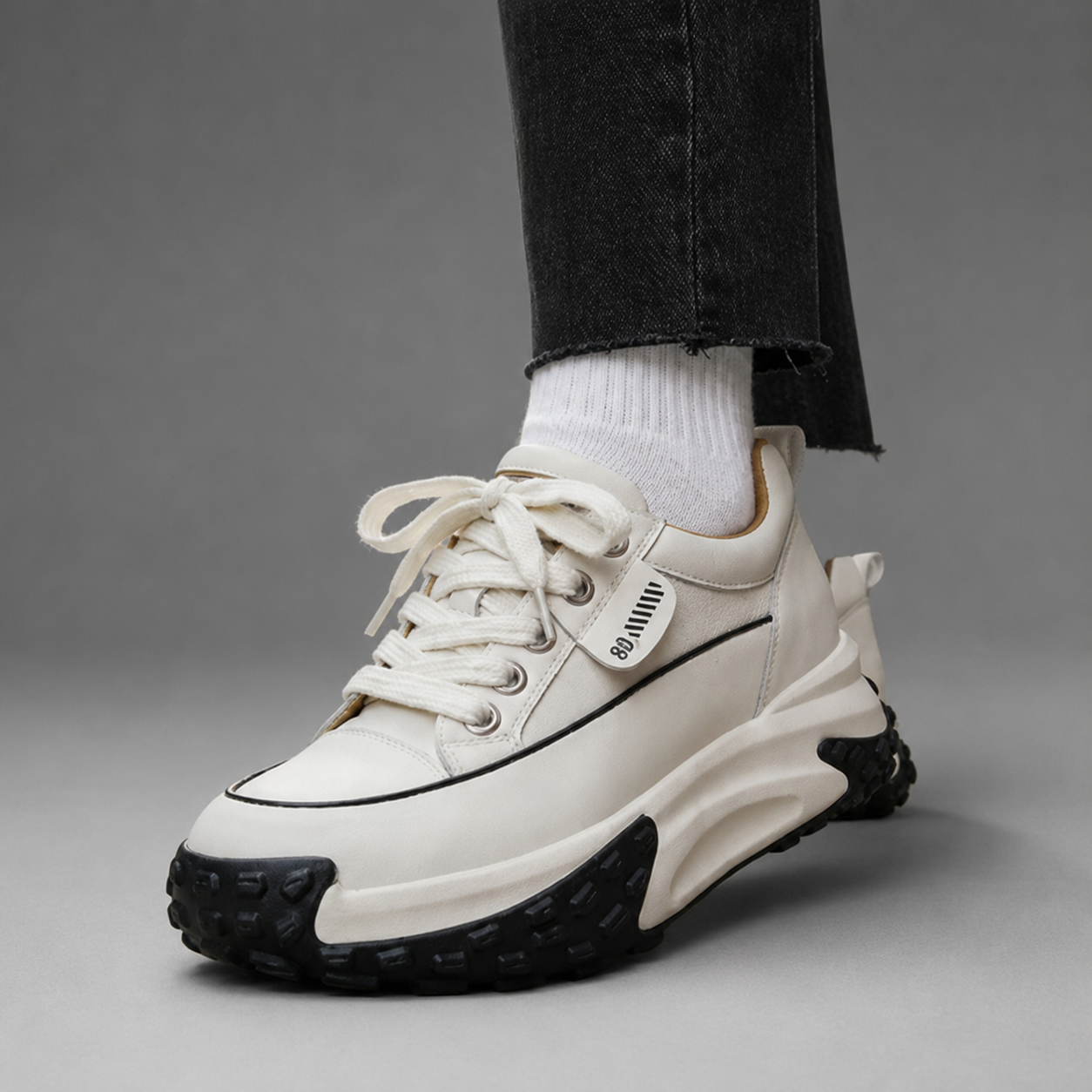 White sneaker with black sole worn by a person on a gray background